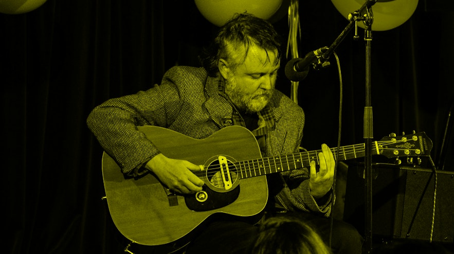Person sitting on stage, holding an acoustic guitar