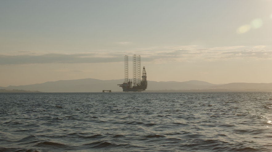 A silhouette of an oil rig in the distance on a deep blue sea.